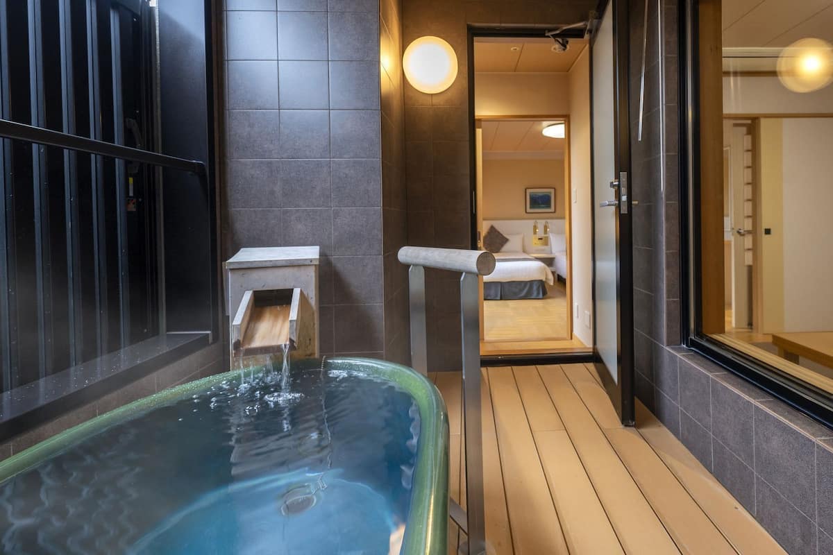 A spa area with a hot tub, wooden flooring, and a view into a bedroom.