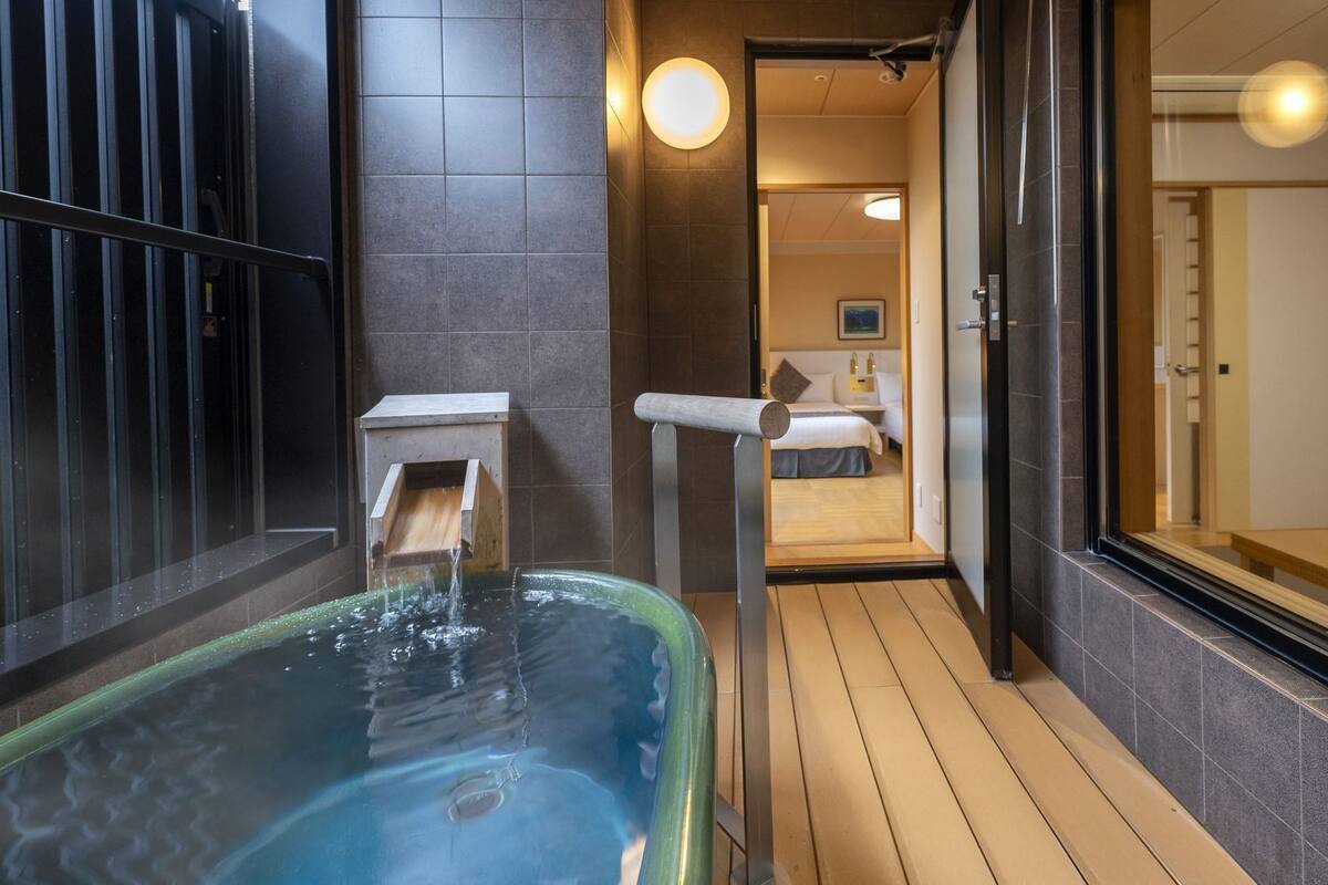 A spa area with a hot tub, wooden flooring, and a view into a bedroom.