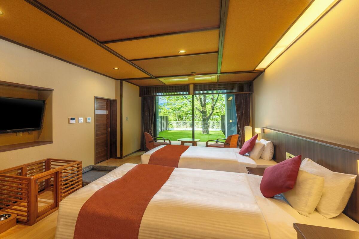 A hotel room with two beds, a TV, a wooden crib, and a view of a garden.