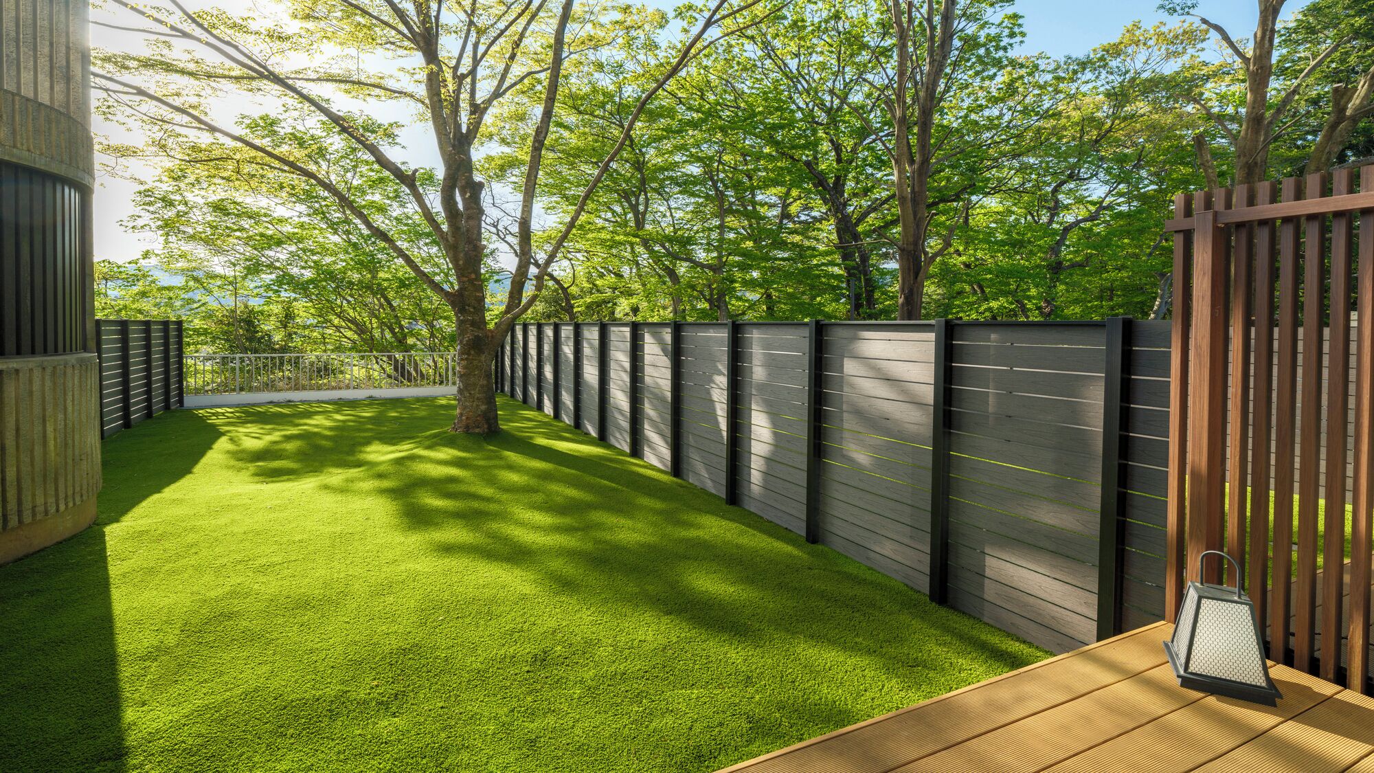 A neatly maintained backyard with artificial grass, a wooden deck, and a metal fence.