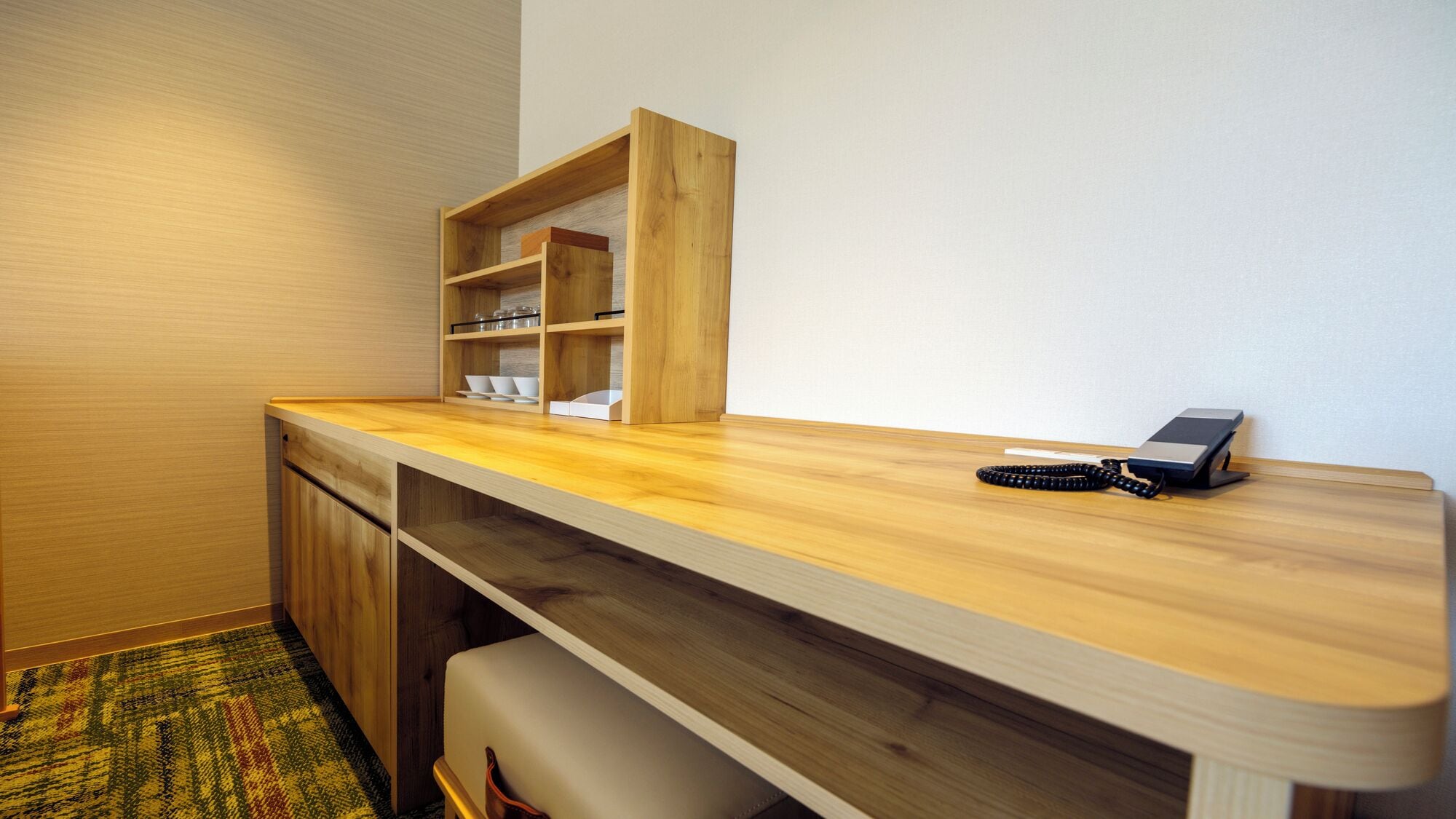 Een kleine hotelkamer met een houten bureau, een telefoon en ingebouwde opbergplanken.