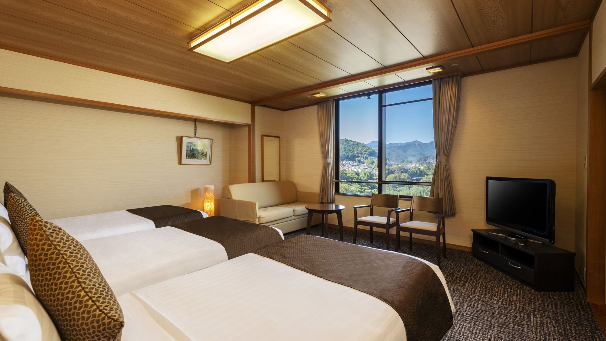 A hotel room with two beds, a sofa, a TV, and a view of a mountainous landscape.