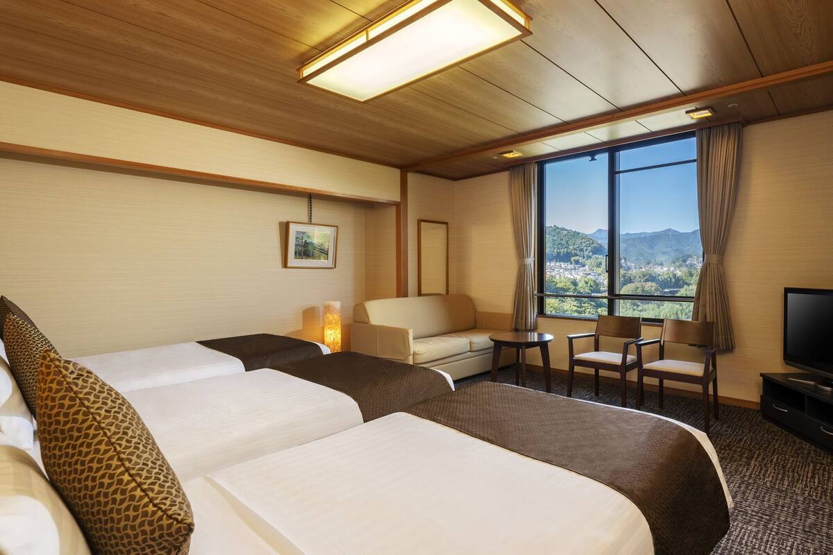 A hotel room with two beds, a sofa, a TV, and a view of a mountainous landscape.
