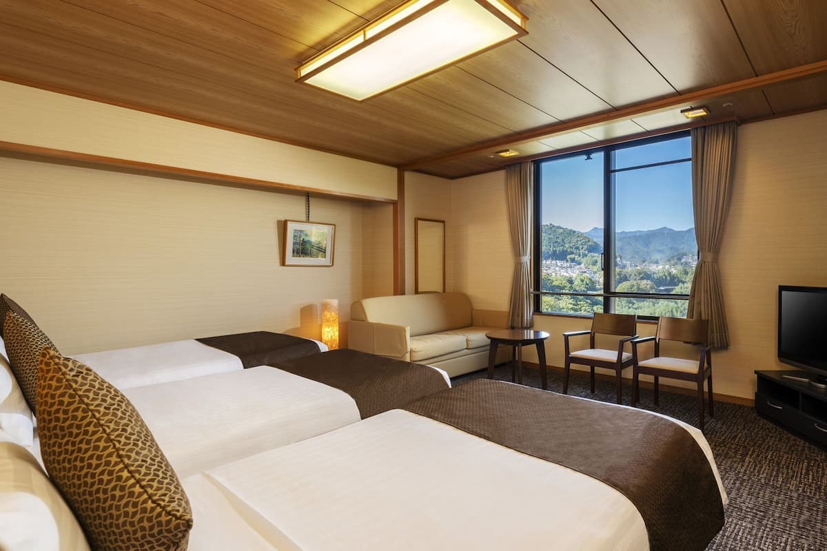 A hotel room with two beds, a sofa, a TV, and a view of a mountainous landscape.