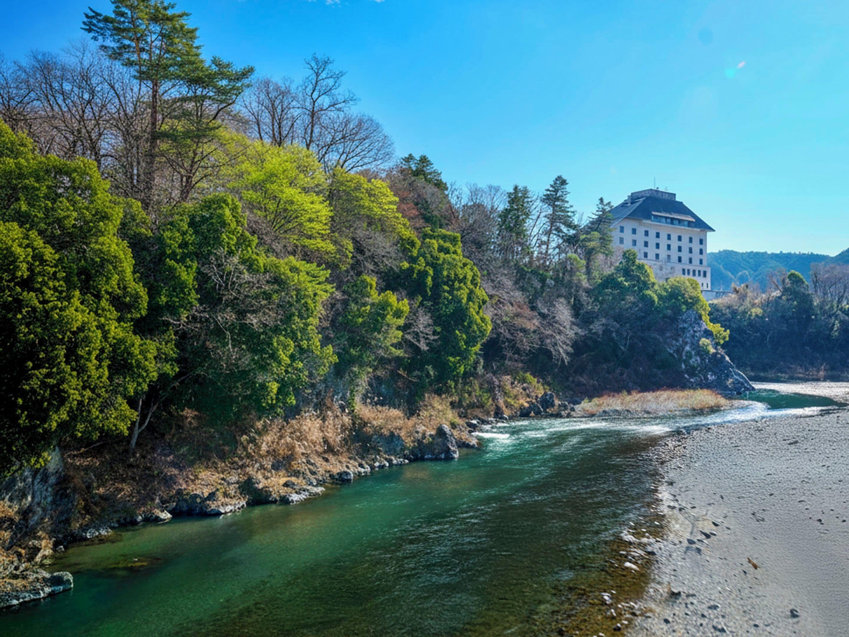 Un río fluye junto a un edificio de fachada amplia y blanca con numerosas ventanas.