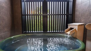 Een spa-ruimte met een groot, groen bad, een houten bankje en uitzicht door een metalen hek.