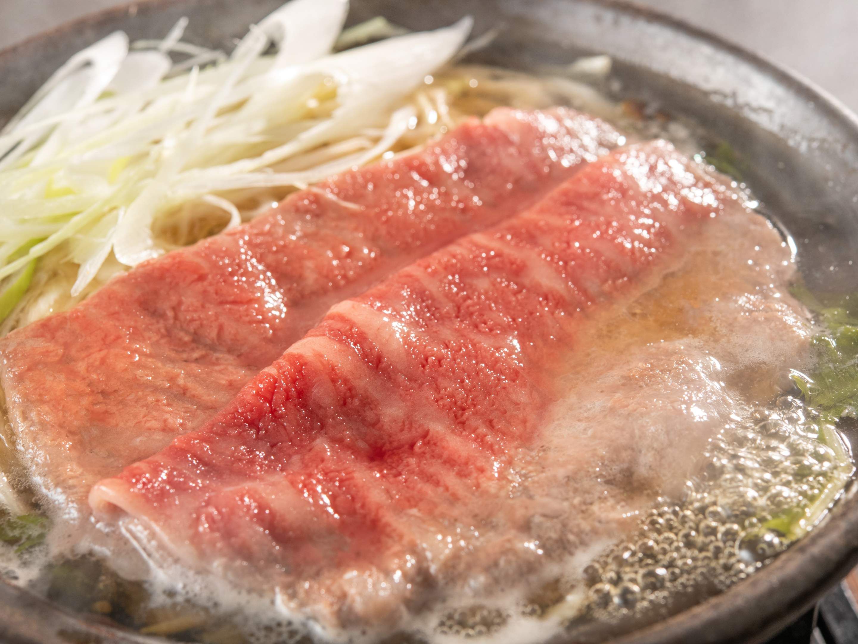 A pan with a piece of salmon cooking in a broth, accompanied by sliced vegetables.