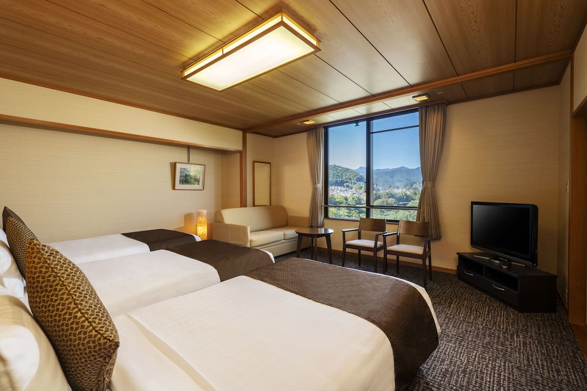A hotel room with two beds, a sofa, a TV, and a view of a city and mountains.