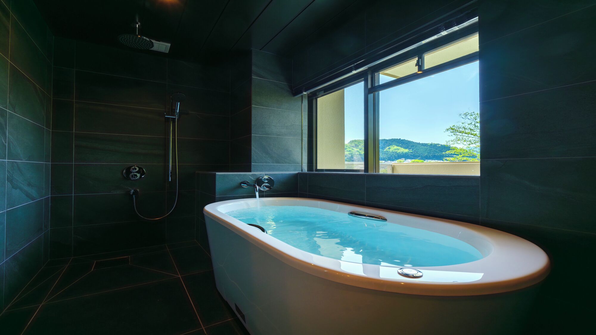 Un baño moderno con una bañera independiente, zona de ducha y un amplio ventanal con vistas al exterior.