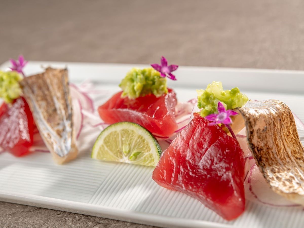 A plate with various food items, including slices of red fish and a lime wedge.