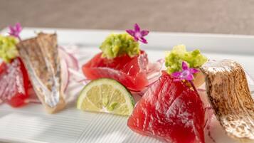 A plate with various food items, including slices of red fish and a lime wedge.
