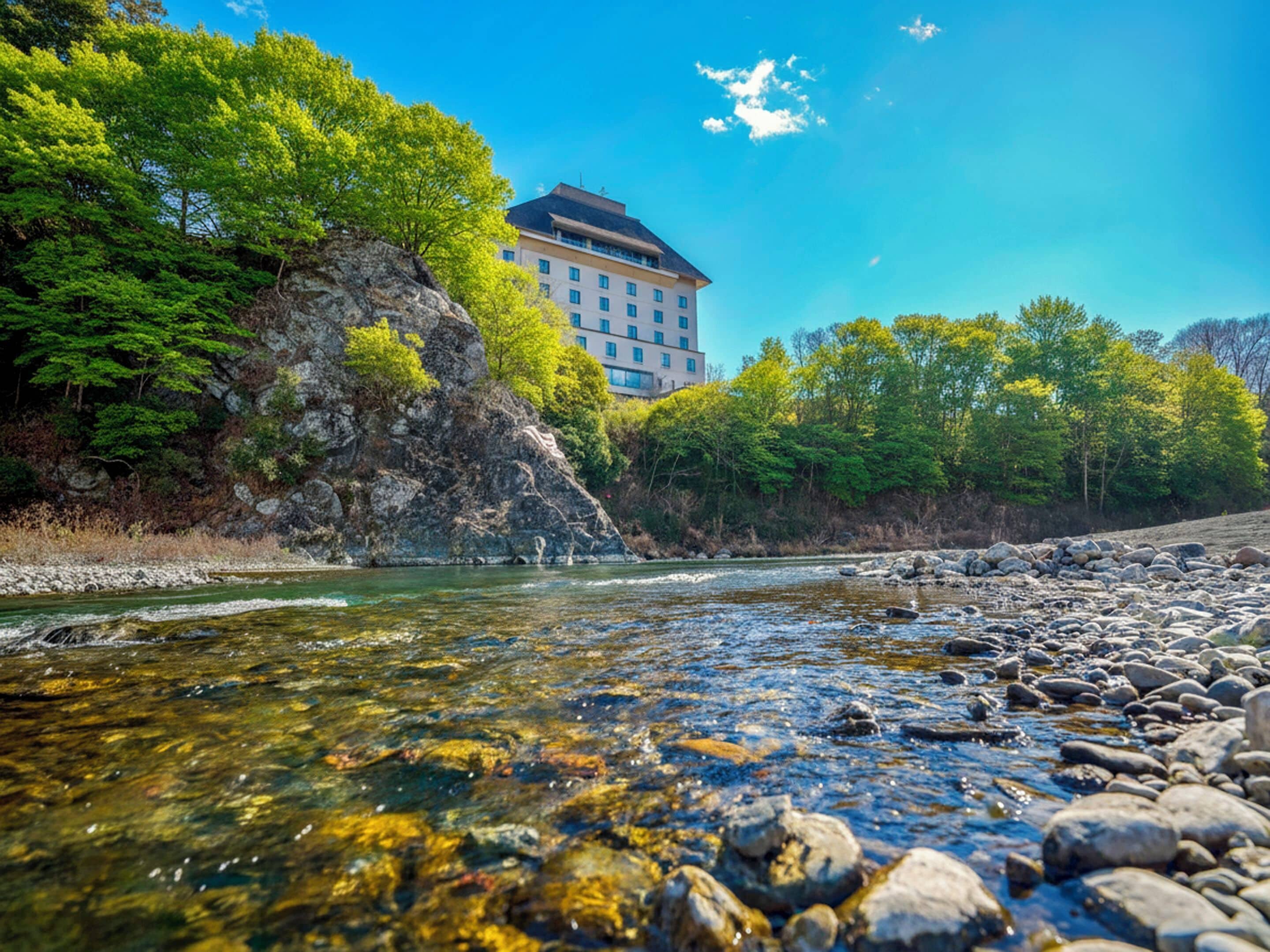 Un río de aguas transparentes, rodeado de rocas y vegetación, con un edificio al fondo.