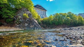 A river with clear water, surrounded by rocks and greenery, with a building in the background.