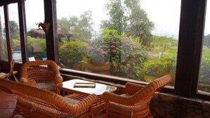 A room with wicker furniture, a glass table, and a view of a garden with various plants and flowers. - Maddiola Apart 2, Orio (Orio)