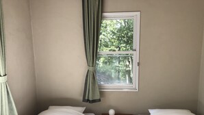 A room with two single beds, a window with curtains, a small wooden nightstand, and a view of trees outside. - Pension Jamoo (Yamanakako)