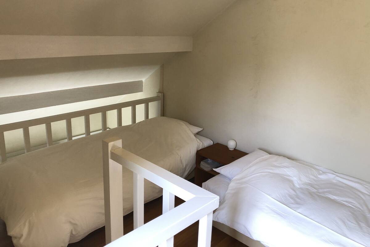 A small, single-bed room with a sloped ceiling and a white railing.
