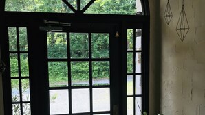 A door with a view of a green landscape, a potted plant, and a wall with geometric decorations. - Pension Jamoo (Yamanakako)