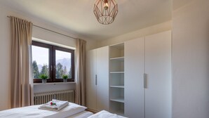 Ein Schlafzimmer mit zwei Betten, einem Fenster mit Vorhängen, einem Heizkörper und einem Kleiderschrank mit Ablageflächen.