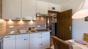 Eine moderne Küche mit weißen Schränken, einer Spüle aus Edelstahl und einer Holz Arbeitsplatte. An der Wand hängt eine Uhr und eine Tür führt in einen anderen Raum.