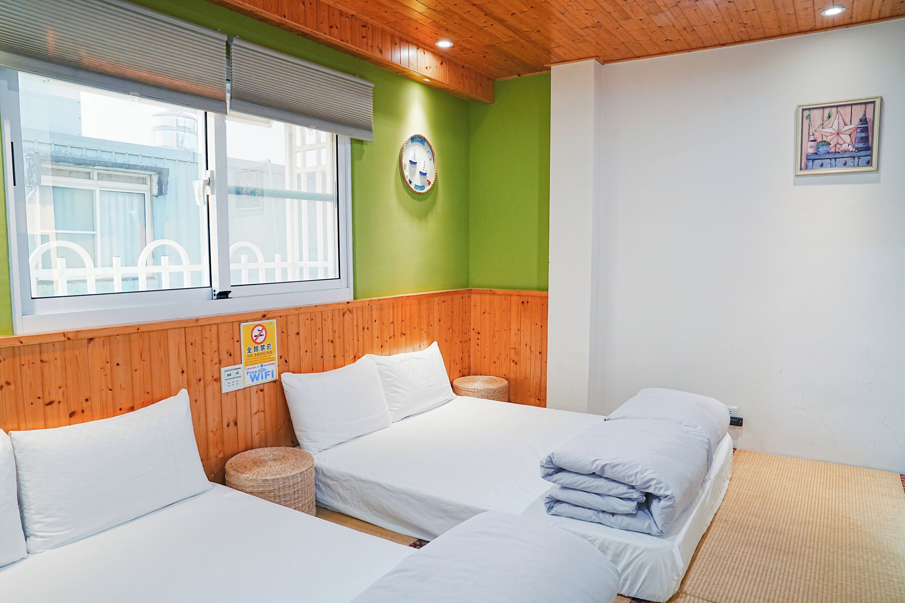 A hotel room with three beds, a wooden ceiling, a green wall, and a window with blinds.