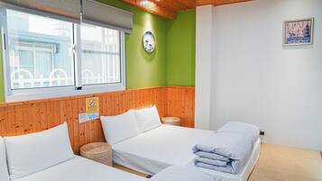 A hotel room with three beds, a wooden ceiling, a green wall, and a window with blinds.