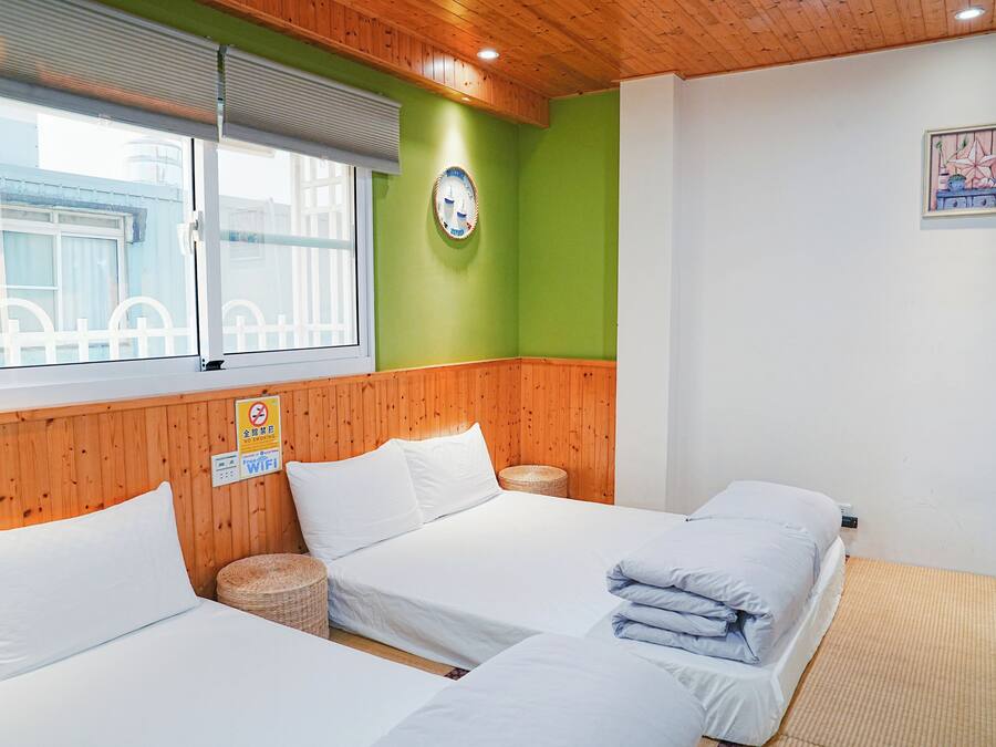 A hotel room with three beds, a wooden ceiling, a green wall, and a window with blinds.