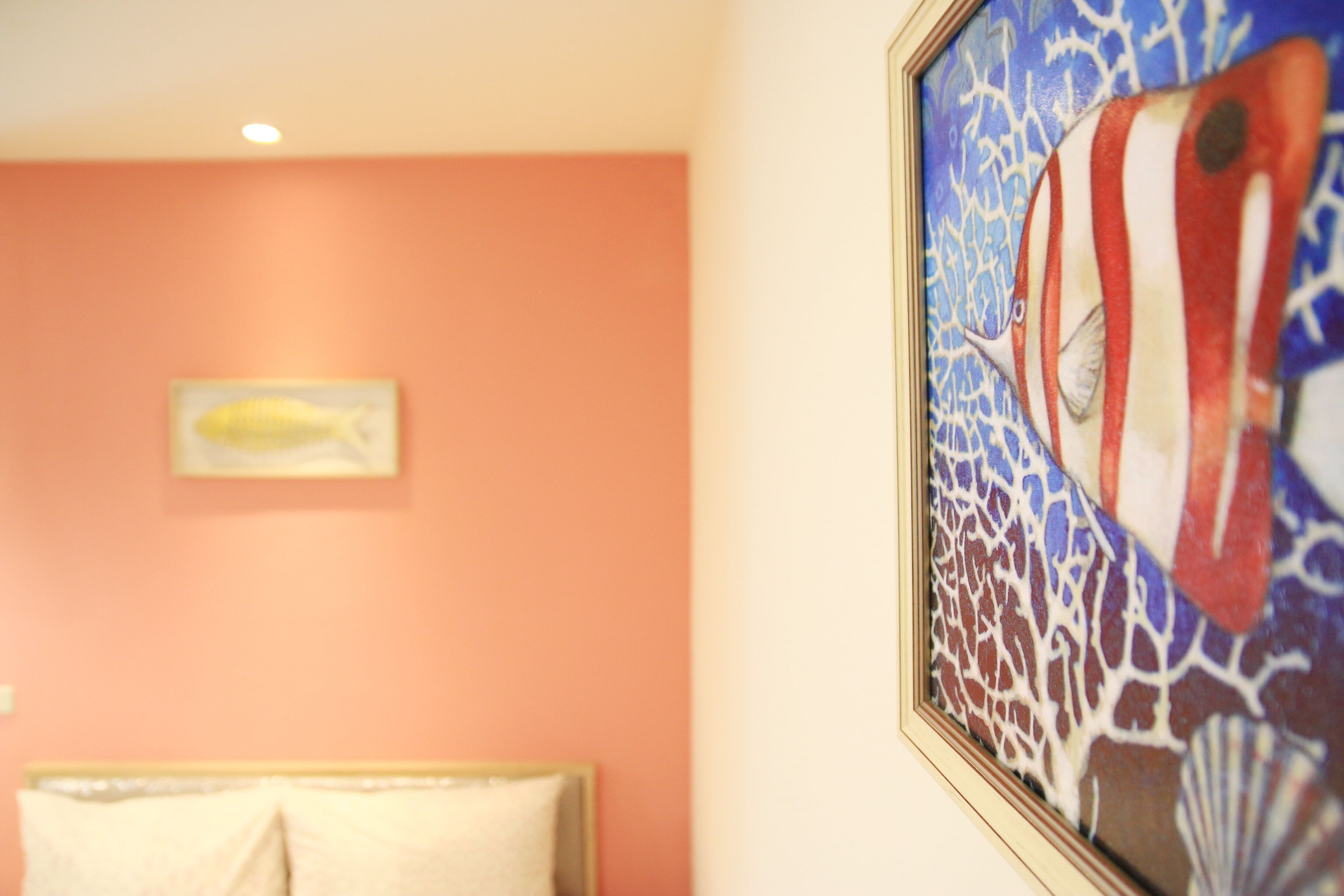 Une chambre avec un lit, un tableau encadré représentant un poisson et un mur décoré d’un motif de récif corallien.