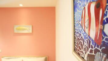Une chambre avec un lit, un tableau encadré représentant un poisson et un mur décoré d’un motif de récif corallien.