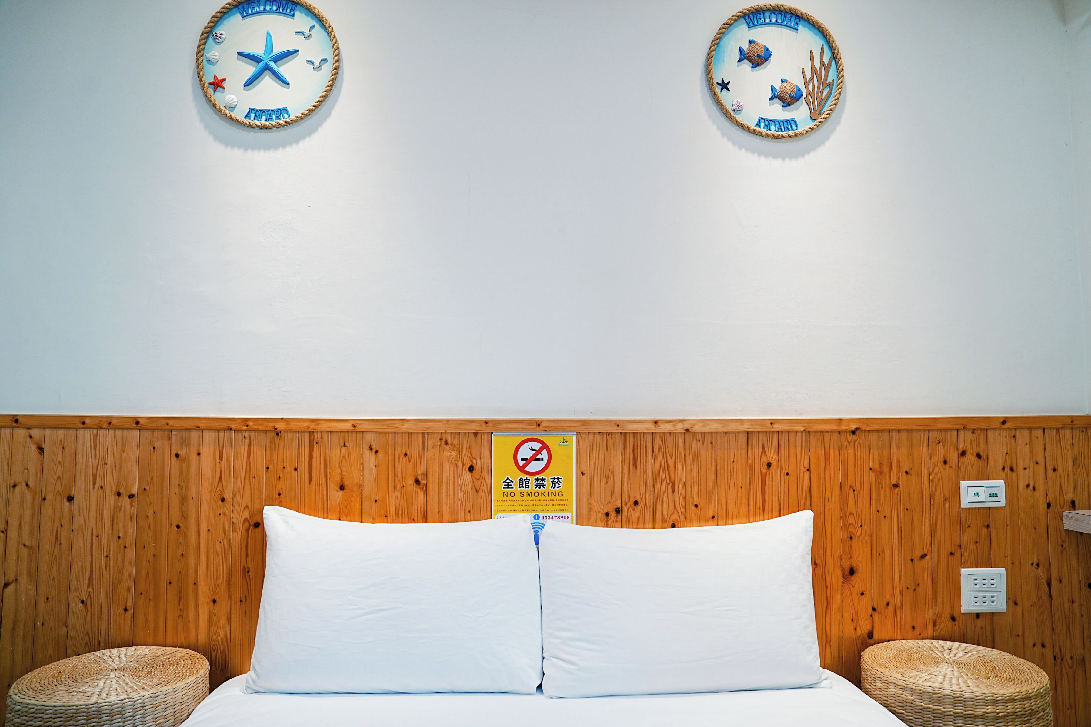 A hotel room with a wooden headboard, two round wall decorations, a no-smoking sign, and a bed with white bedding.