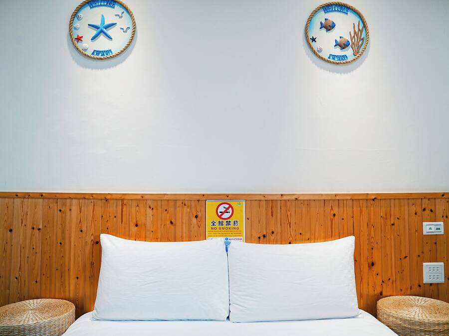 A hotel room with a wooden headboard, two round wall decorations, a no-smoking sign, and a bed with white bedding.
