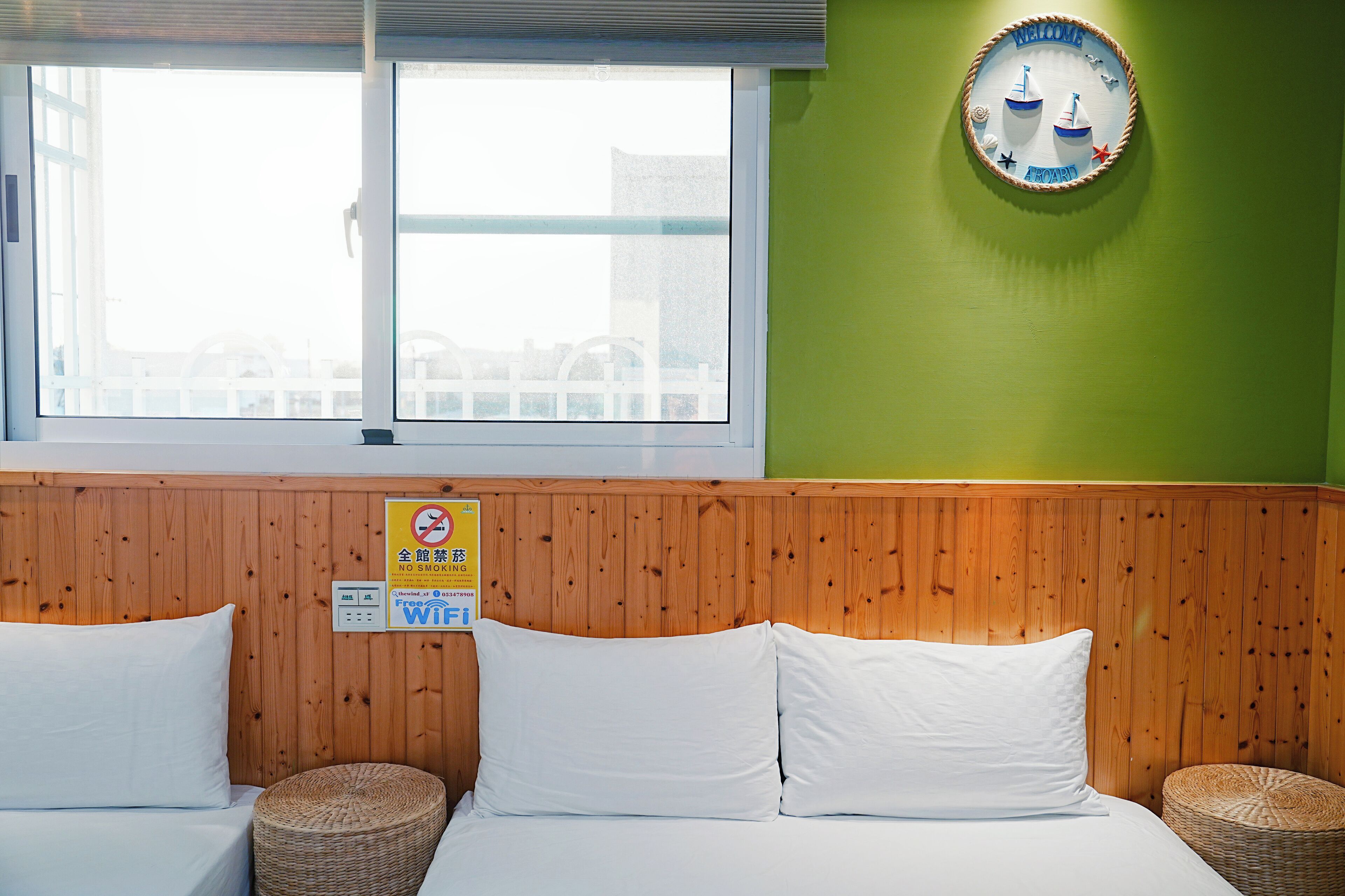 A hotel room with a bed, two pillows, a wooden headboard, a window, and a welcome sign.