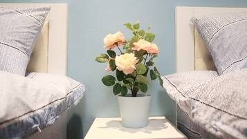 A bed with a white headboard, a small white nightstand with a potted plant, and a light blue wall.