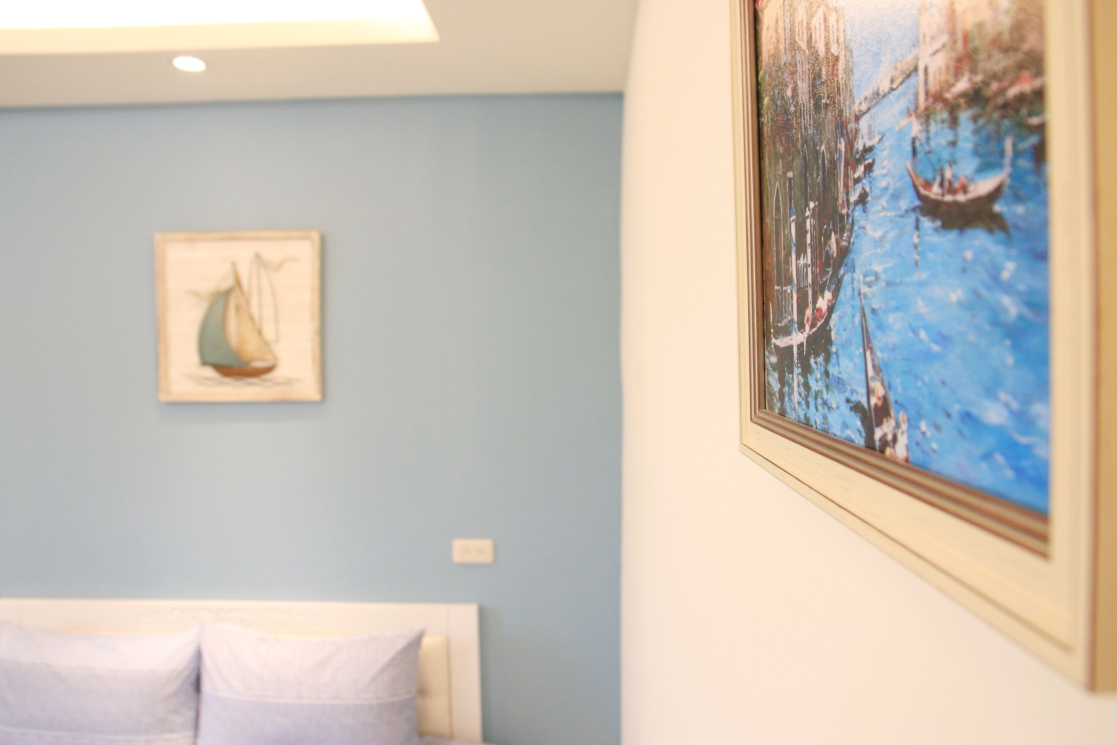 Une chambre à coucher avec un lit, un tableau représentant un voilier accroché au mur et une photographie encadrée d’un paysage de canal.