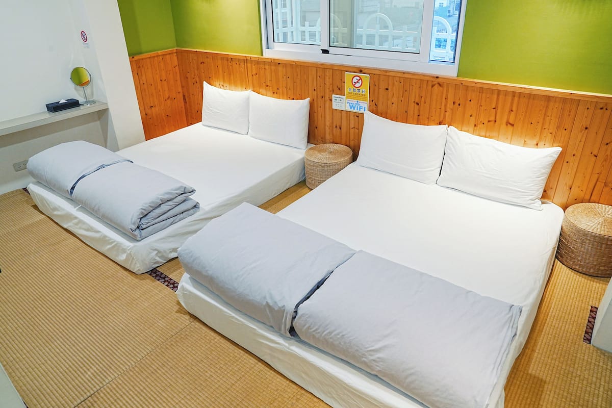 Une chambre d’hôtel avec deux lits, une tête de lit en bois, une fenêtre avec vue, un panneau indiquant la présence d’une connexion Wi-Fi et une petite table avec une lampe.