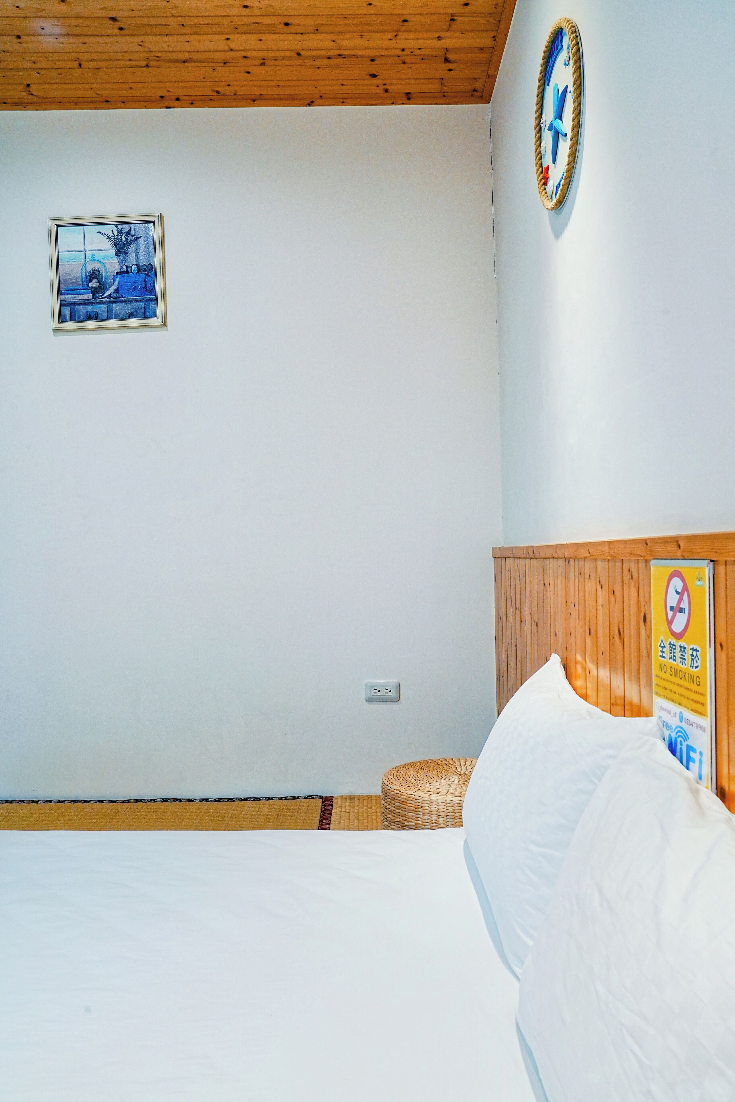 A bedroom with a bed, a framed picture on the wall, a no-smoking sign, and a wooden ceiling.