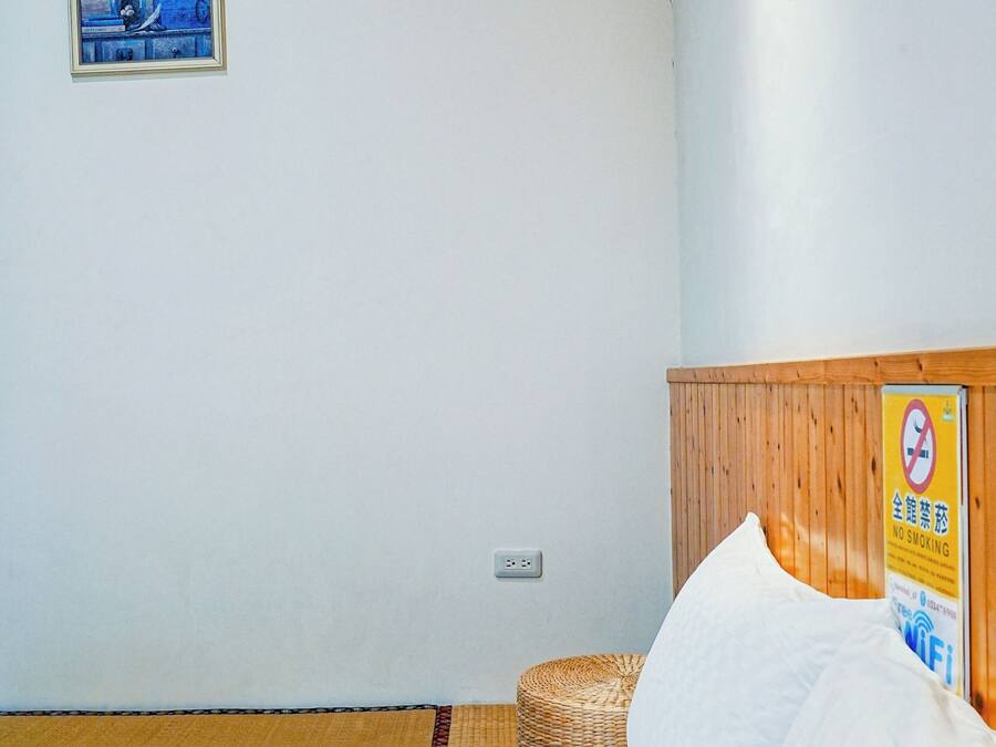 A bedroom with a bed, a framed picture on the wall, a no-smoking sign, and a wooden ceiling.