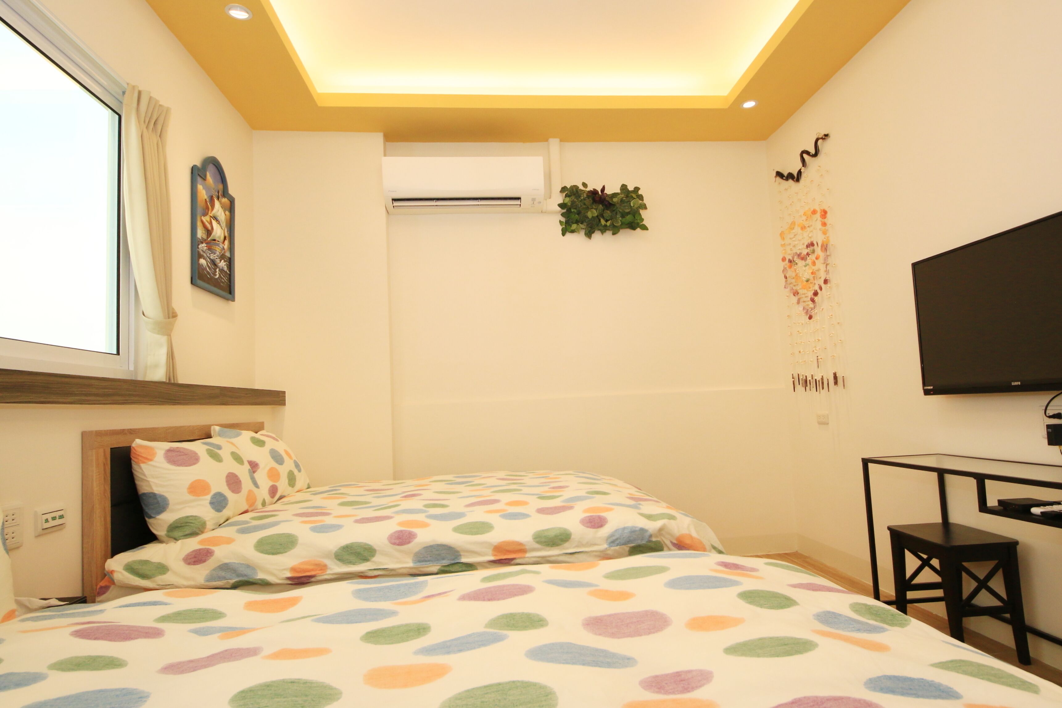 A bedroom with two beds, a TV, a desk, and a window with curtains.