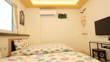 A bedroom with two beds, a TV, a desk, and a window with curtains.