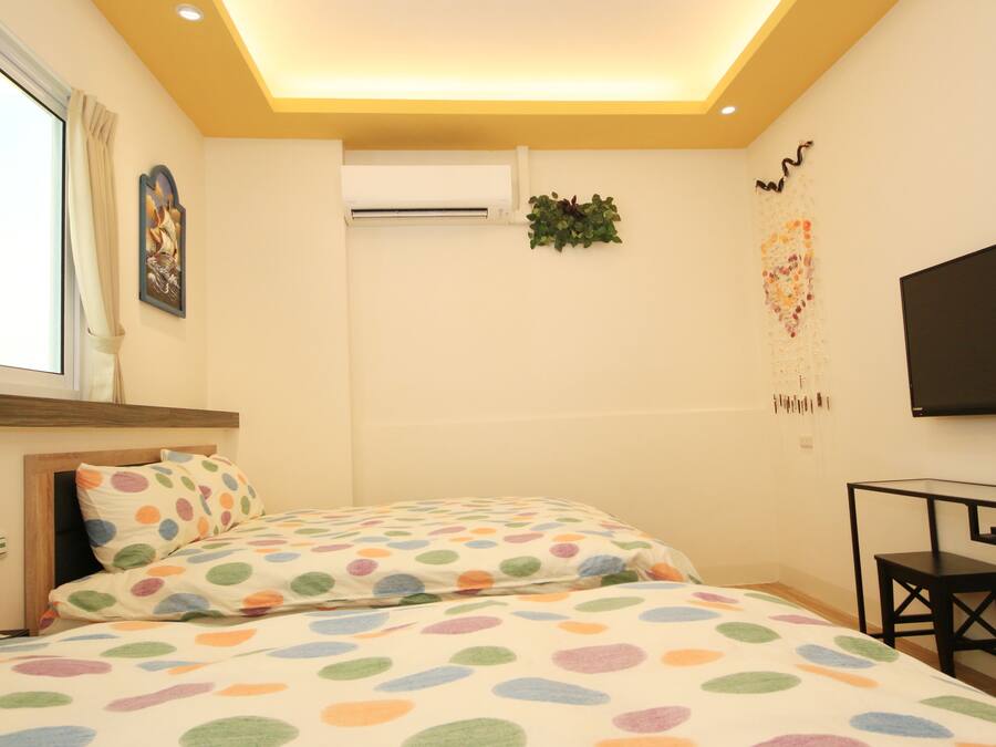 A bedroom with two beds, a TV, a desk, and a window with curtains.