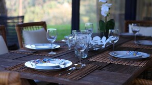 Mesa lista con platos, vasos y una jarrón, con vistas a la vegetación.