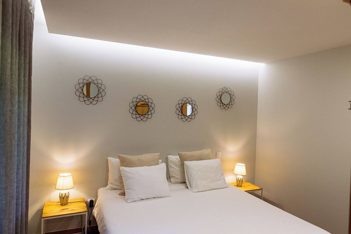 A neatly arranged bedroom with a large bed, two bedside tables with lamps, and three wall-mounted mirrors.