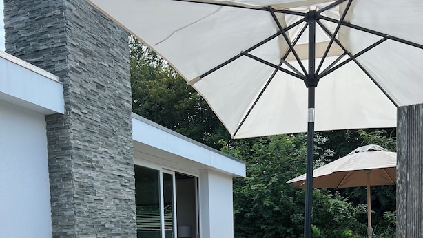 Un espacio exterior con asientos, una pared de piedra, un sofá y una mesa con sombrilla.