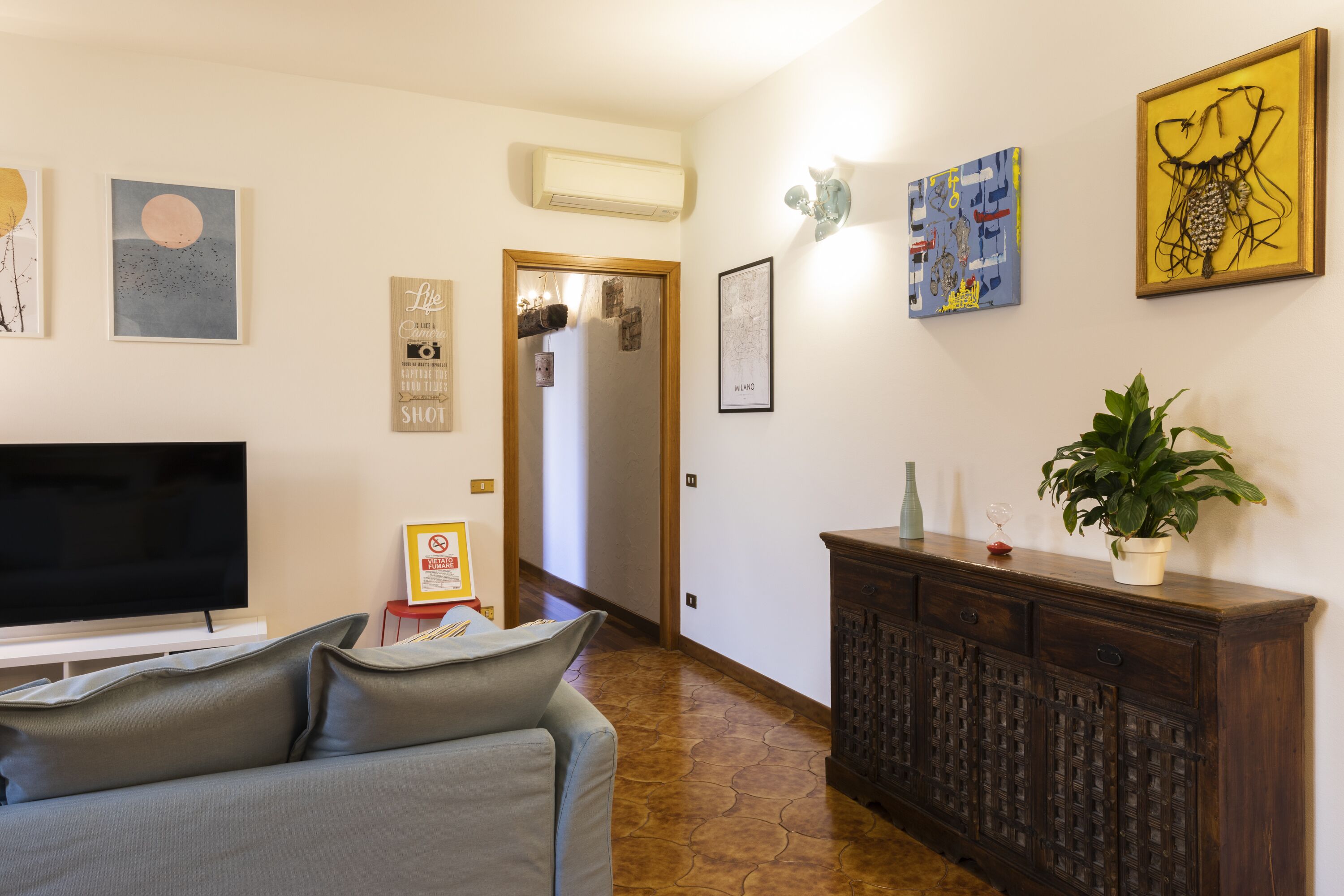 Una sala de estar con un televisor de pantalla plana, un sofá gris, un mueble de madera y varias obras de arte en la pared.