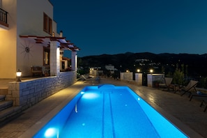 A swimming pool with a stone wall and steps leading up to it, surrounded by lounge chairs and a pergola.
