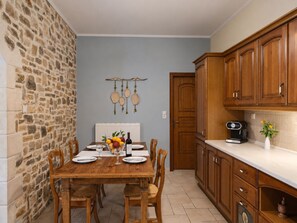 A dining area with a stone wall, wooden table, chairs, and a fruit bowl.