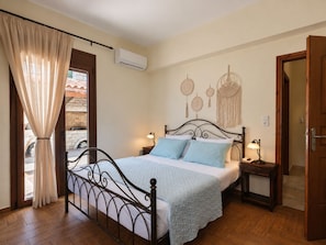 A bedroom with a bed, bedside tables, a window with curtains, an air conditioning unit, and a wall with decorative items.