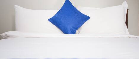 A bed with white bedding and a single blue pillow.