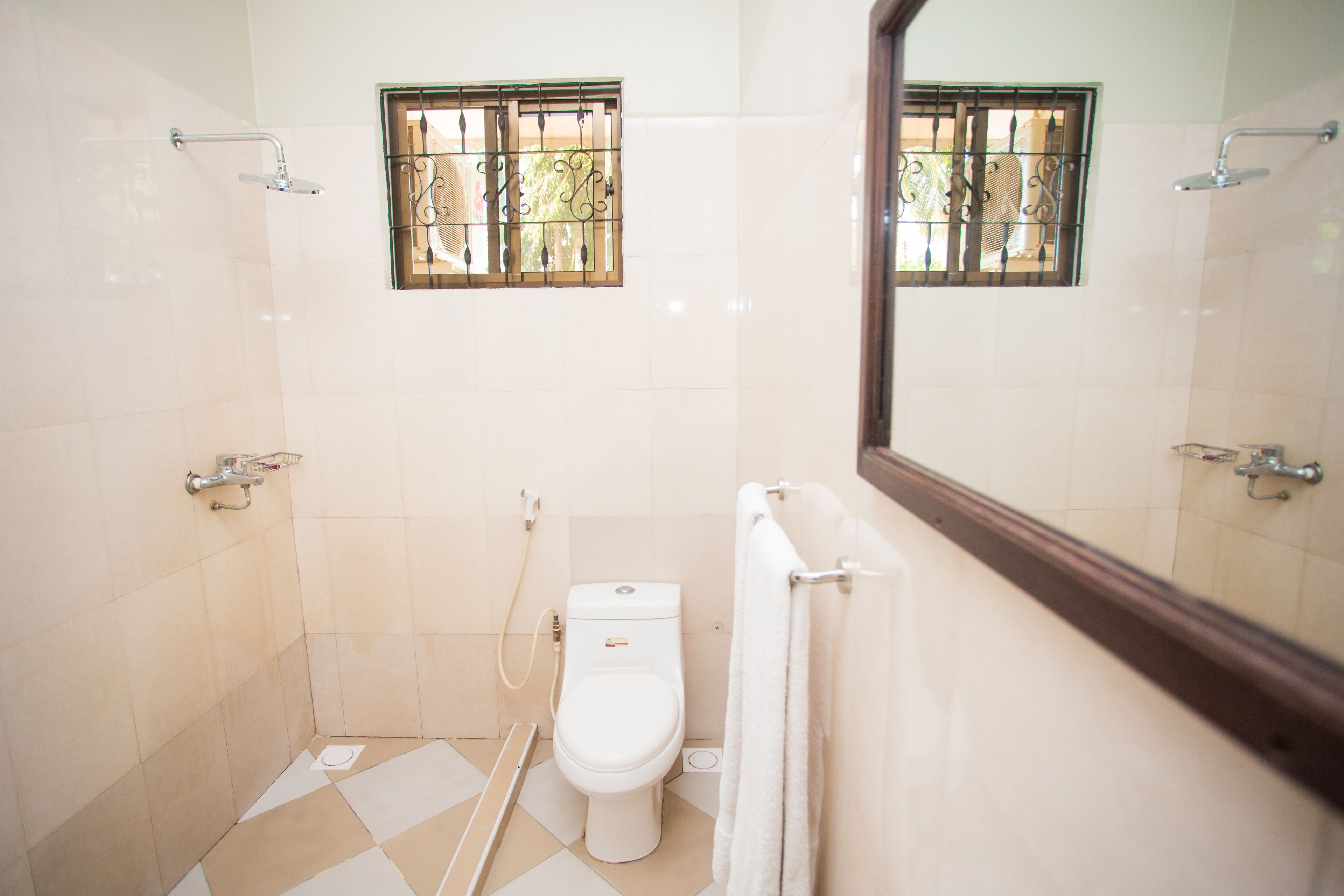 Un baño pequeño y limpio con inodoro, ducha y ventana con rejas.