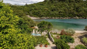 Un paisaje costero con una vista despejada de una playa, una piscina pequeña y un sendero que lleva a una estructura de piedra.