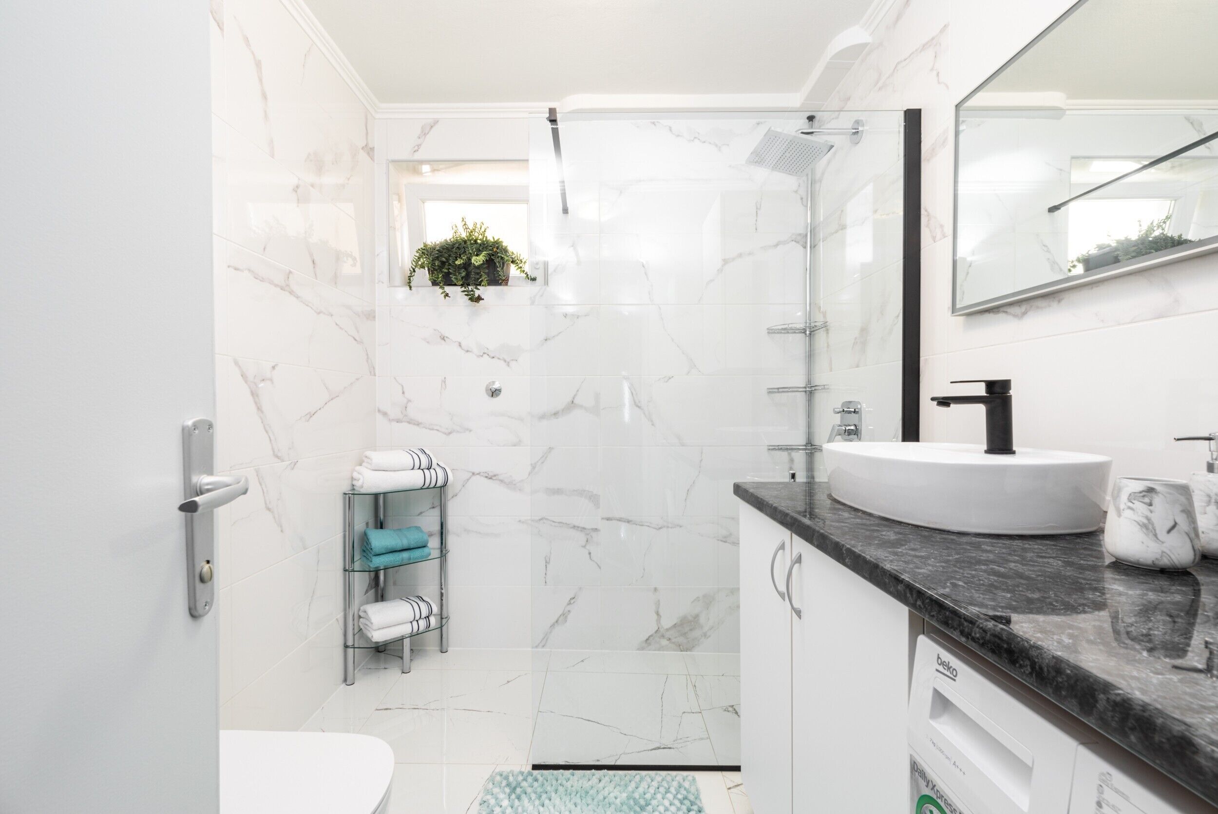A modern bathroom with a white sink, black countertop, and a glass shower enclosure.
